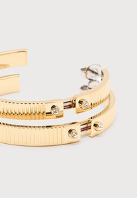 Σκουλαρίκια κρίκοι σε χρυσαφί απόχρωση με ριμπ ύφανση, μικρές καθαρές πέτρες και ασημί πεταλούδα κούμπωμα σε λευκό φόντο.