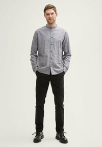 Chemise grise à col rabattu avec devant à boutons et manches longues, associée à un pantalon noir et des chaussures montantes noires. Tissu lisse, coupe décontractée.
