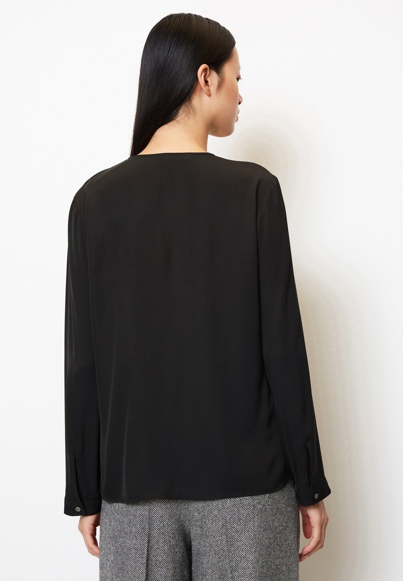 Czarna bluzka z długim rękawem o gładkiej fakturze, okrągłym dekolcie i mankietach na guziki, zestawiona z szarymi spodniami w wzór houndstooth.