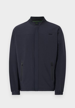 Veste zippée bleu marine avec col montant, poignets élastiques, deux poches latérales zippées, motif vertical subtil et petit logo sur la poitrine.