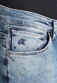 Light blue denim jeans featuring a rear pocket with embroidered "OK" logo. The fabric has a worn texture with subtle fading.