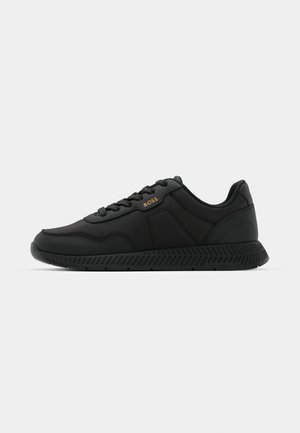 Black athletic sneakers with a smooth textile upper, rubber sole, and subtle embossed detailing. Features lace-up design and minimal branding.