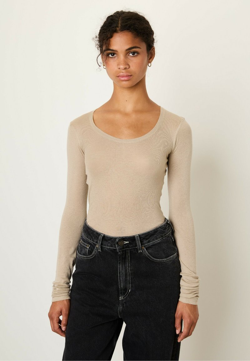 Beige long-sleeve top with a scoop neckline made of textured fabric, paired with high-waisted black jeans featuring contrast stitching and pockets.