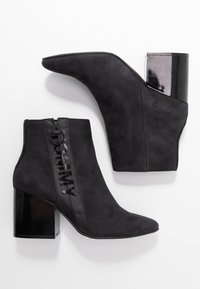 Botas de tobillo negras con acabado de ante, que cuentan con un tacón de bloque negro brillante y una cremallera lateral adornada con el logo "TOMMY."