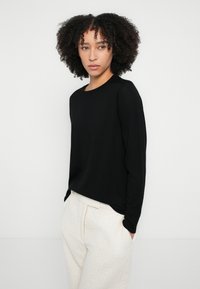 Fekete hosszú ujjú kötött pulóver kerek nyakkivágással, világos bézs texturált nadrággal párosítva. Sima anyag, laza szabás és egyszerű dizájn.