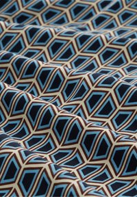 Tissu à motifs présentant des formes géométriques emboîtées en bleu, marron et crème, avec une texture lisse et un éclat raffiné.