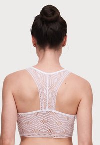 Bralette bianco in pizzo con un motivo geometrico, design a schiena scoperta con finitura testurizzata e bordi in elastico.