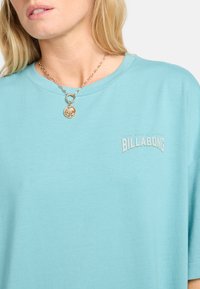 Világoskék pamut póló kerek nyakkivágással, rövid ujjakkal és egy kis szürke "Billabong" logóval. Egyszerű dizájn, minta nélkül.