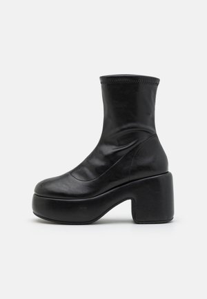 Melnas ādas potītes zābaki ar biezāku platformu un taisnstūra papēdi, gluda virsma un nedaudz stiepjams augšējais šafts.