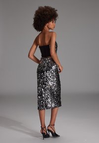 Robe noire sans bretelles avec un corsage ajusté et une jupe recouverte de sequins argentés. Le mannequin porte des sandales à talons et de grandes boucles d'oreilles créoles.