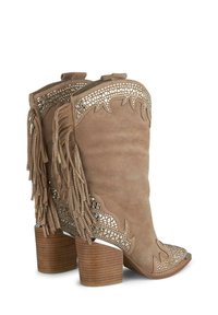 Bottines en suede marron clair avec un design découpé complexe, des franges et un talon en bois empilé. Bout angulaire et accents texturés.
