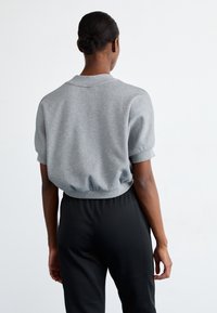 Felpa grigia a maniche corte con collo arrotondato e orlo elastico, abbinata a pantaloni neri. Tessuto liscio con vestibilità comoda.