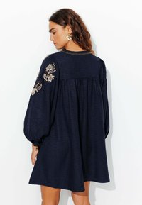 Robe bleu marine à manches longues et bouffantes, ornée d'une broderie florale élaborée sur les épaules et d'un design de dos froncé.