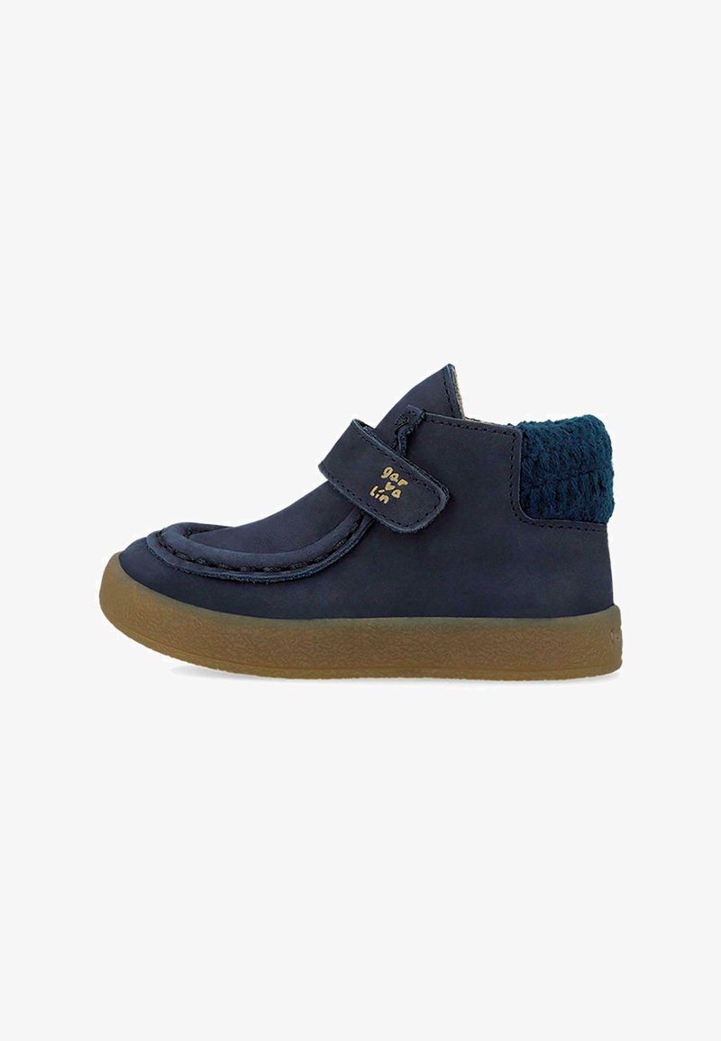 Botas de cuero azul marino con un cuello de punto texturizado azul, correa de velcro y suela de goma marrón. Presenta una punta redondeada y acentos de costura.