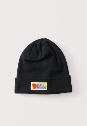 Czarna dzianinowa czapka z podwiniętym brzegiem z prostokątną żółtą naszywką z czerwonym logo lisa i niebieskim tekstem "Fjallraven".