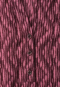 Gros plan sur un tissu zébré bordeaux et rose avec trois petits boutons foncés sur une patte verticale.