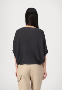 Grafitowoszary oversize'owy top z fakturowanym wzorem dzianiny, krótkimi rękawami i szerokim dekoltem, w połączeniu z beżowymi spodniami z wysokim stanem.