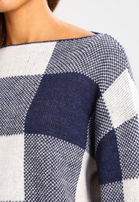 Sweter wykonany z plecionki, z wzorem w kratę, w granatowo-kremowych odcieniach. Materiał ma teksturowane wykończenie, idealne na chłodniejsze dni.