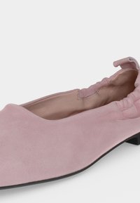 Chaussure plate en daim rose doux avec un dos élastiqué et une doublure intérieure en cuir beige, montrée en gros plan sous un angle latéral.