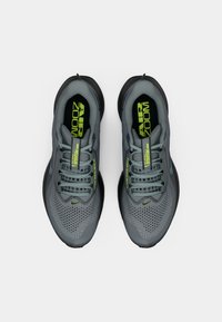Pár sivých bežeckých topánok Nike Air Zoom Pegasus s textilným zvrškom, čiernymi podrážkami a detailmi neonovo žltej farby, pozorované zhora.