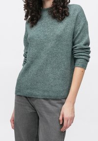 Gebreide, lichtgroene trui met een ronde hals en opgerolde mouwen, gemaakt van een zachte breistof. Gecombineerd met grijze spijkerbroek.