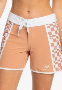 Persika badshorts med vit midja, som har ett rutigt mönster och blommor som dekoration. Inkluderar dragsnodd och kontrasterande vit kant.