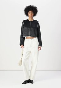 Black cropped satin jacket with long sleeves and white piping, paired with high-waisted white trousers and black pointed-toe heels.