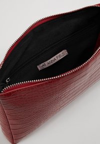 Rød kosmetiktaske med krokodilleprægning, sort stofindvendigt, med lynlåslukning og en indvendig lomme mærket "ANNA FIELD."