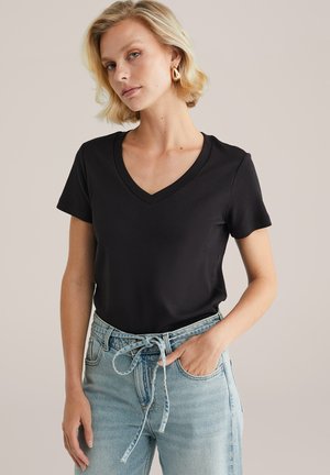 T-shirt nera con collo a V realizzato in tessuto liscio, maniche corte, abbinata a jeans a vita alta blu chiaro con dettaglio in vita legato.