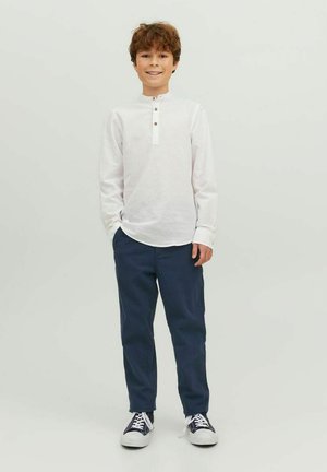 Maglietta henley bianca a maniche lunghe con plastron bottonato; abbinata a pantaloni chinos blu navy e sneakers bianco e nere. Design semplice e casual.