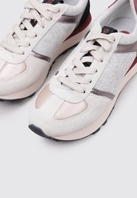 Baskets beige clair en cuir suédé et mesh, avec des accents roses, des superpositions texturées et un capuchon de talon noir. Design à lacets avec semelle en caoutchouc.