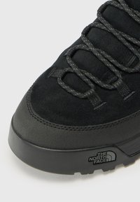 Czarne buty trekkingowe z górnej części wykonanej z zamszu i gumy, z misternym sznurowaniem, grubą podeszwą oraz z logo blisko pięty.