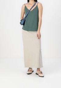 Top in tessuto a scallop verde, gonna lunga a coste beige e scarpe chunky chiare. Borsa a tracolla blu che aggiunge contrasto. Texture piatte e lisce.