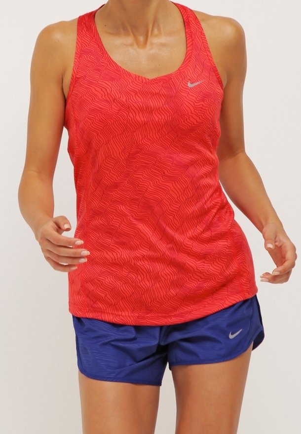 Débardeur de sport rouge à motif ondulé, associé à un short bleu. Les deux présentent des logos Nike dans des couleurs subtiles et contrastées. Texture lisse.