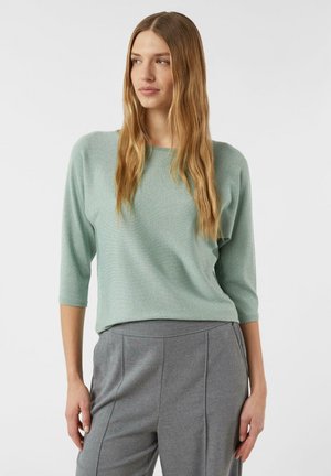 Miętowozielony teksturowany top z rękawami do połowy łokcia i luźnym krojem, zestawiony z szarymi, dopasowanymi spodniami.