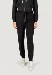 Czarne dresy o zwężającym się kroju z elastycznymi mankietami, z wiązaniem w pasie i miękkim materiałem. Połączone z białymi trampkami.