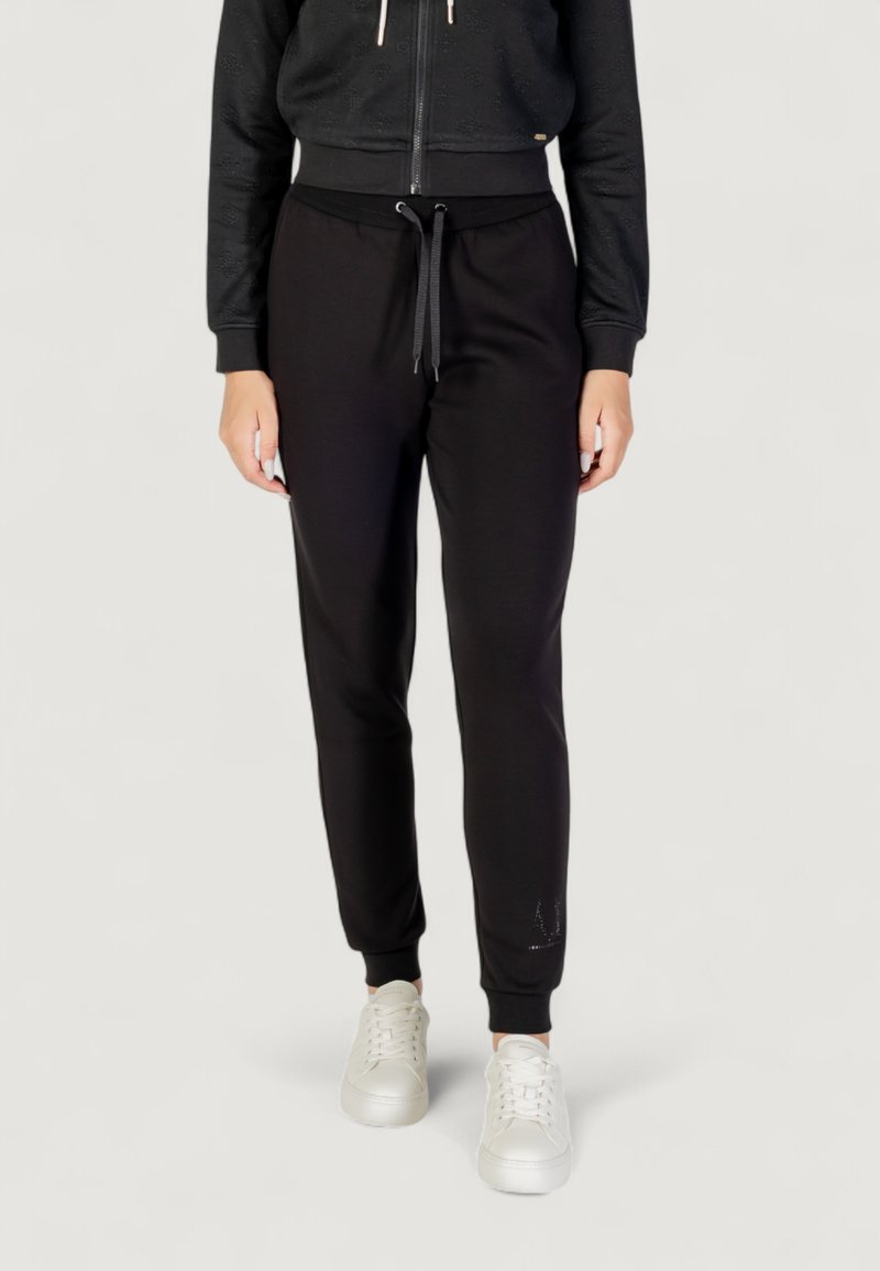Czarne dresy o zwężającym się kroju z elastycznymi mankietami, z wiązaniem w pasie i miękkim materiałem. Połączone z białymi trampkami.