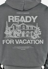 Dos d'un sweat à capuche gris avec un graphisme blanc représentant une maison de style méditerranéen, des arbres et le texte "Ready for vacation" et "Moments to memories."
