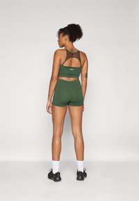 Zöld sportos melltartó és shorts szett, hálós háttal, testihez simuló kialakítással és diszkrét márkalogóval a derékpánton.