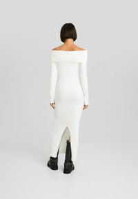 Vit stickad klänning med bar axel, långa ärmar, ribbad halsringning, smal passform och sidssprund. Matchad med svarta klumpiga klackstövlar.