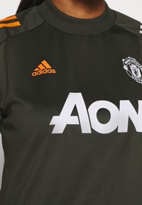 Zielona koszulka Manchester United z białym logo "Aon" i pomarańczowym znakiem Adidas. Posiada okrągły dekolt oraz teksturowany materiał z wzorem siatki.