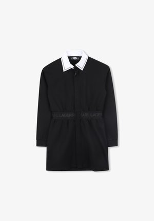 Crna haljina s dugim rukavima, sa bijelim ovratnikom i pojasom u struku. Izrađena od glatkog materijala s suptilnim brendiranjem.