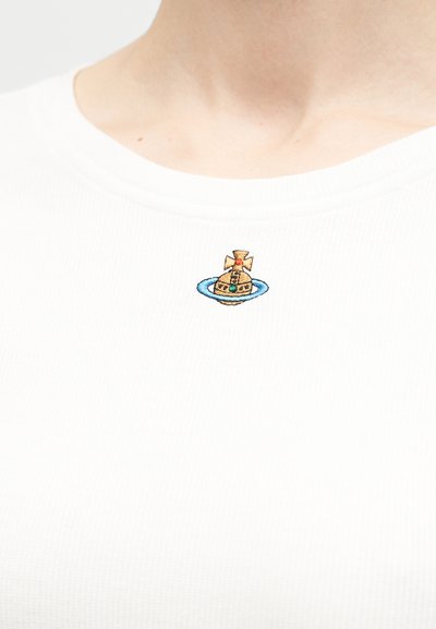 Λευκό πουκάμισο με μικρό κεντημένο έμβλημα χρυσαφένιας σφαίρας με σταυρό στην κορυφή, περιβαλλόμενο από μπλε δακτύλιο, τοποθετημένο στο κέντρο κοντά στον γιακά.