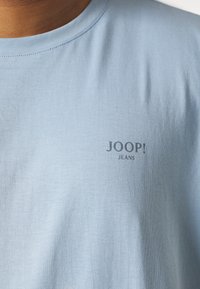 T-shirt azzurro a maniche corte in cotone con una superficie liscia, dotato di un piccolo logo grigio scuro "JOOP! JEANS" sul petto.