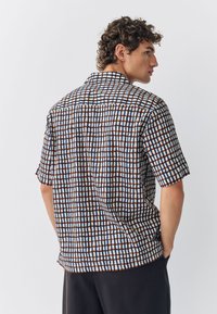 Camicia a maniche corte con un motivo a griglia multicolore in blu, marrone e bianco; realizzata in tessuto leggero; vestibilità comoda con colletto.