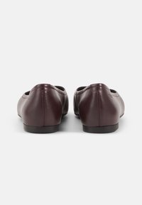 Ballerines en cuir bourgogne avec bout rond, semelle plate et texture lisse. Détails de couture le long du talon et des côtés.