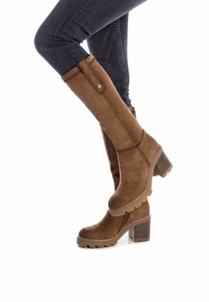 Botas marrones hasta la rodilla, hechas de ante, con un tacón grueso y apilado, que cuentan con un zip lateral y costuras de contraste a lo largo de los bordes.