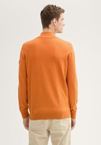 Oranges Strickpullover mit langen Ärmeln und geripptem Saum. Verfügt über einen klassischen Kragen und ein einfaches Design, hergestellt aus weichem Material.