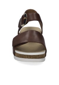 Hnědá kožená sandála s překříženými popruhy, kruhovým kovovým sponou, korekovo tím a bílou gumovou podrážkou.