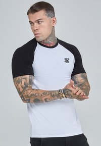 Camiseta de manga corta tipo ragl�án con cuerpo blanco y mangas negras. Presenta un pequeño logotipo negro en el pecho y un diseño ajustado.